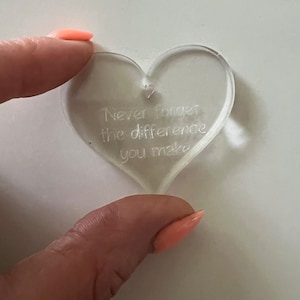 2 fingers holding a clear heart that reads "never forget the difference you make" with a small heart shaped hole at the top