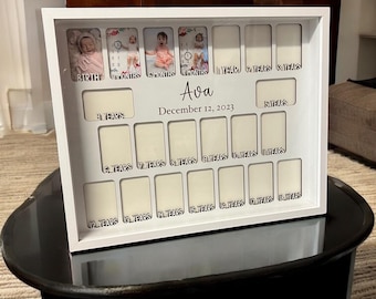 May include: A white rectangular photo frame with multiple slots for growth milestones. The frame features the name Ava and the date December 12, 2023, with labels ranging from birth to 18 years. Some slots contain baby photographs.