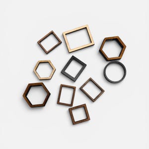 May include: A collection of small, hollow wooden frames in various geometric shapes, including squares, rectangles, hexagons, and a circle. The frames feature different wood tones ranging from light tan to dark brown and black, with visible wood grain.