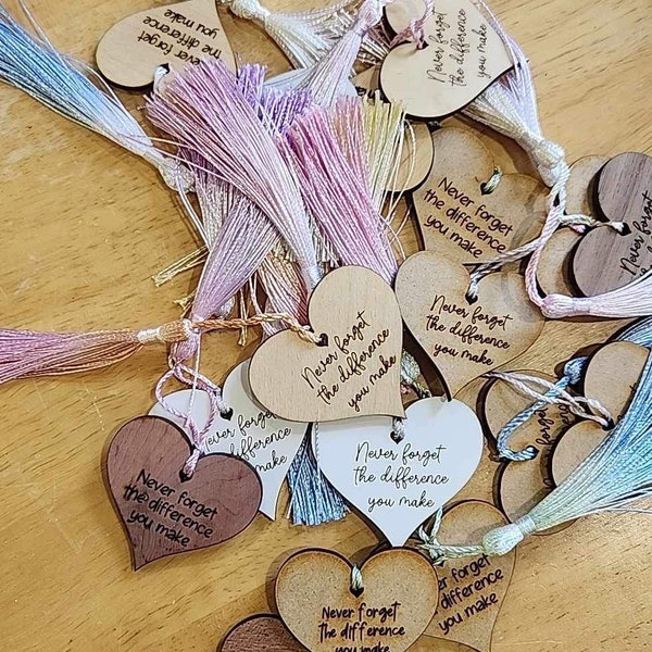 May include: A collection of wooden heart-shaped ornaments with the phrase "Never forget the difference you make" inscribed on them. Each ornament has a colorful tassel attached.
