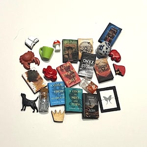 May include: A collection of miniature book charms, a green mug, a mushroom, a black dog, a crab, a crown, and other small decorative items. The books have titles like "A Court of Thorns and Roses" and "Iron Flame".