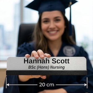 May include: A desk nameplate, 20 cm wide, with the name "Hannah Scott" and "BSc (Hons) Nursing" printed in black. The nameplate is held by a person wearing a graduation gown and cap.