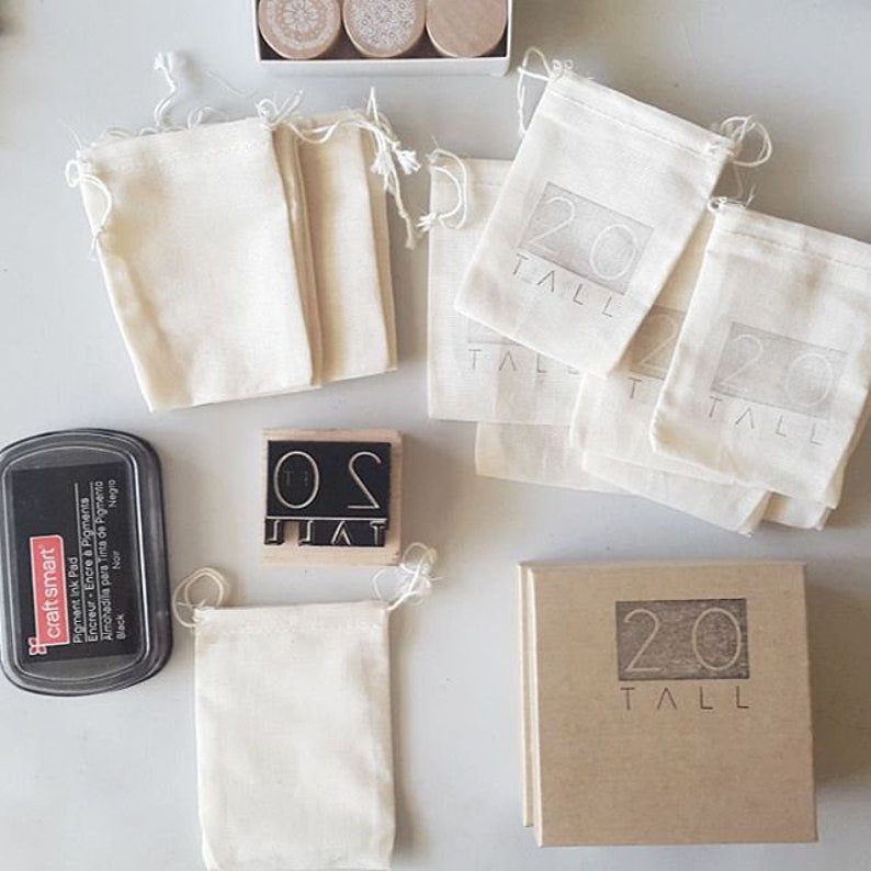 May include: A selection of craft items featuring a black ink pad, a wooden stamp with the text "SO TALL", and several small canvas bags. Some bags are printed with the text "20 TALL". Wooden stamps are also included in a box.