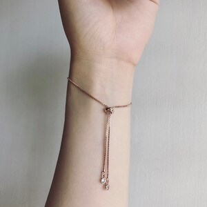 May include: Rose gold adjustable bracelet with a delicate chain and two dangling clear crystals. The bracelet features a sliding knot closure for a customizable fit. A simple and elegant piece of jewellery.