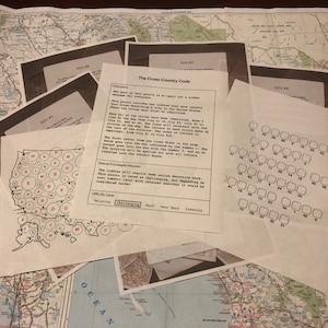 Può includere: Una raccolta di fogli su uno sfondo di mappa. I fogli includono un puzzle con il testo "The Cross Country Code", una mappa con lettere e una griglia di caselle. Il livello di difficoltà è indicato come "Challenging".