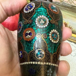 May include: A small, decorative vase with a green, black, and gold cloisonn&eacute; design. The vase is hand-painted with intricate details and features a mosaic-like pattern.