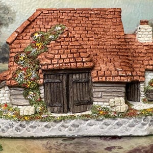 May include: A miniature cottage figurine with a red brick roof, wooden doors, and a stone base. The cottage is adorned with climbing plants and small flowers, creating a charming, rustic aesthetic. A small chimney is visible.