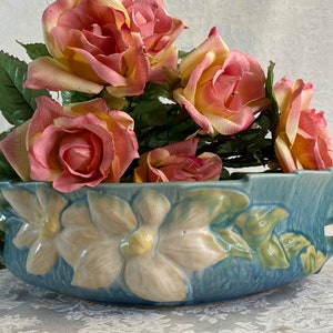 May include: A blue and white ceramic planter with two handles and a floral design. The planter is filled with pink and yellow roses.