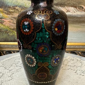 May include: A black and green cloisonn&eacute; vase with a floral design. The vase is decorated with gold and silver accents and features a variety of colorful gemstones.