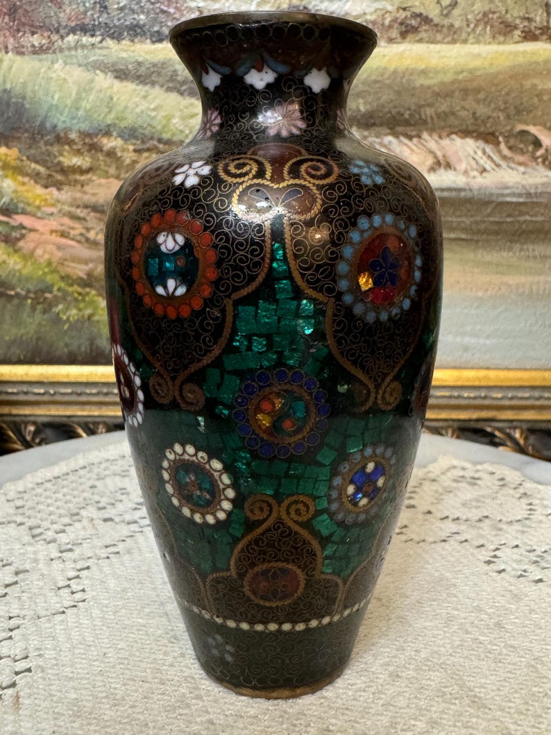 May include: A black and green cloisonn&eacute; vase with a floral design. The vase is decorated with gold and silver accents and features a variety of colorful gemstones.