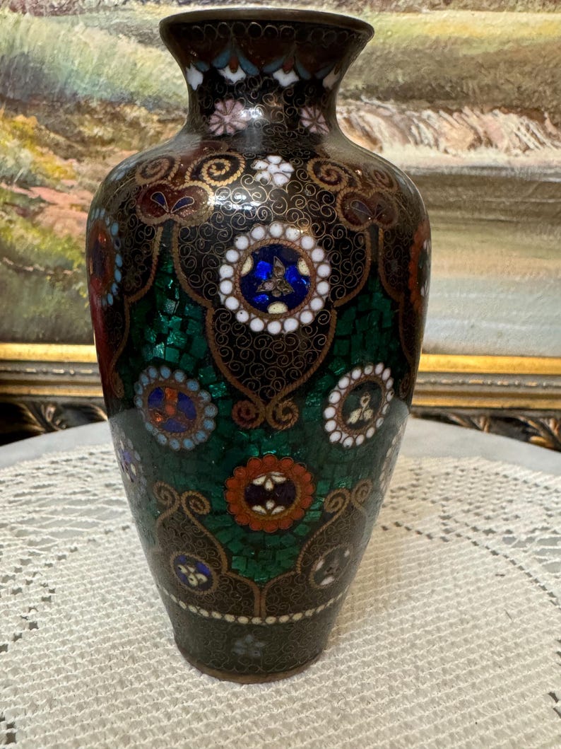 May include: A black cloisonn&eacute; vase with intricate green, blue, red, and white floral patterns. The vase has a round body and a narrow neck.