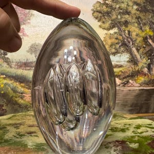 May include: A clear glass paperweight with a rounded oval shape and four internal bubbles. The bubbles are arranged in a vertical row and have a slightly elongated shape.