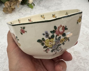 May include: A white ceramic bowl with a green rim and a floral pattern. The bowl is octagonal in shape and has a scalloped edge.