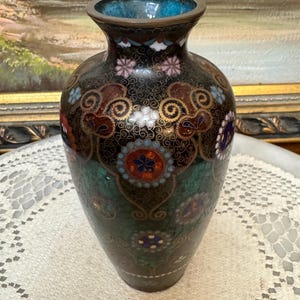 May include: A black and green cloisonn&eacute; vase with a floral design. The vase is decorated with gold, red, white, and blue enamel.