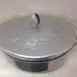 May include: Silver aluminum casserole dish with a lid featuring an embossed tulip design. The lid has a small, decorative tulip finial.