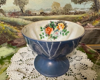 May include: A vintage blue and white ceramic bowl with a floral design. The bowl has a pedestal base and is decorated with a bouquet of roses and leaves.