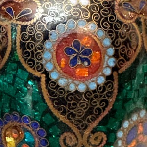 May include: Close-up of a green, black, and gold patterned surface with intricate details. The surface is decorated with small, colorful dots and swirls.