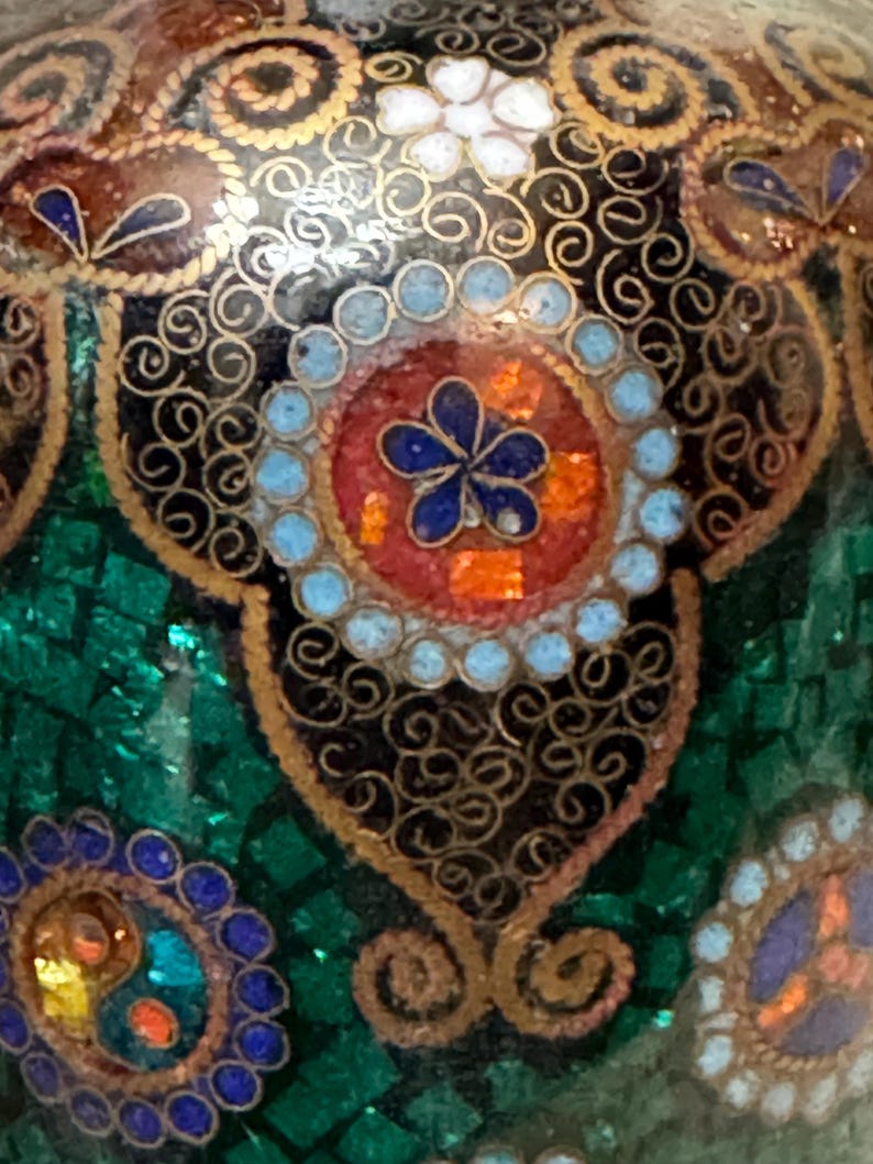 May include: Close-up of a green, black, and gold patterned surface with intricate details. The surface is decorated with small, colorful dots and swirls.