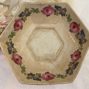 May include: A white octagonal ceramic bowl with a floral design. The bowl has a raised rim and is decorated with pink roses, green leaves, and blue and yellow flowers.