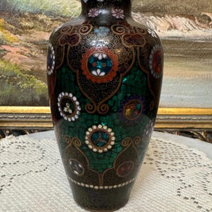 May include: A black and green cloisonn&eacute; vase with a floral design. The vase is decorated with intricate patterns and colorful enamel.