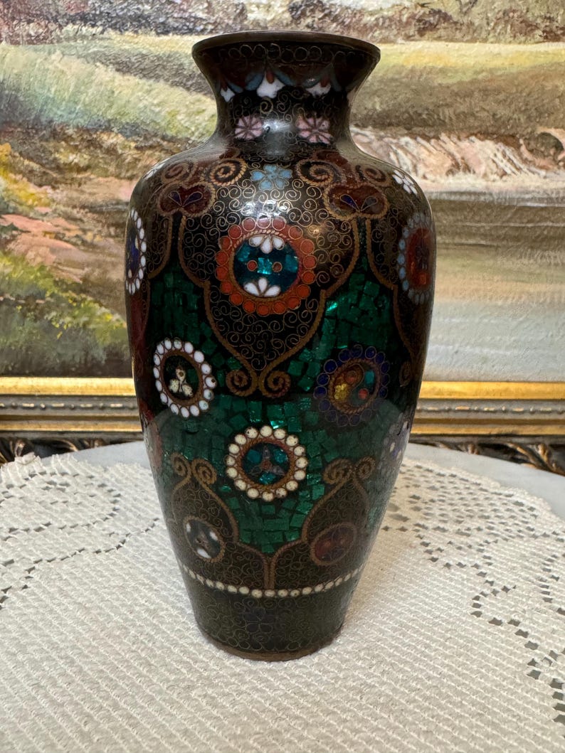 May include: A black and green cloisonn&eacute; vase with a floral design. The vase is decorated with intricate patterns and colorful enamel.