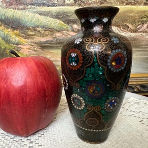 May include: A small, black and green vase with a decorative mosaic pattern. The vase is decorated with gold accents and colorful stones.