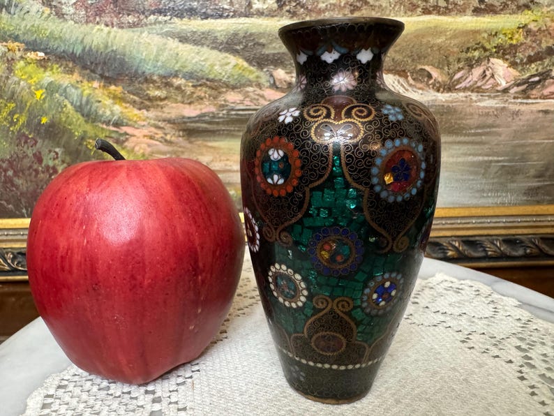 May include: A small, black and green vase with a decorative mosaic pattern. The vase is decorated with gold accents and colorful stones.