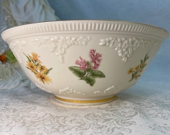 May include: A white porcelain bowl with a gold rim and floral designs. The bowl features three different floral patterns: yellow daisies, pink and white lilacs, and yellow wildflowers.