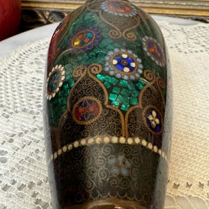 May include: A dark green and gold cloisonn&eacute; vase with intricate floral patterns and colorful accents. The vase is decorated with small, round, mosaic-like pieces of enamel.