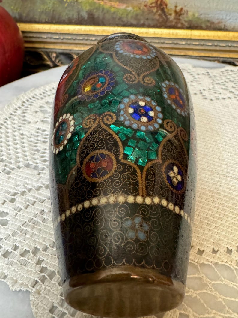 May include: A dark green and gold cloisonn&eacute; vase with intricate floral patterns and colorful accents. The vase is decorated with small, round, mosaic-like pieces of enamel.