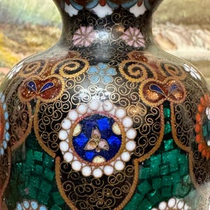 May include: A black cloisonn&eacute; vase with intricate gold and multi-colored floral patterns. The vase has a round body and a narrow neck.