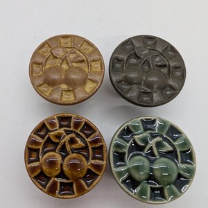Peut inclure: Quatre boutons en céramique avec un motif de cerise. Les boutons sont dans des tons de brun, vert et gris. Chaque bouton a un motif de cerise en relief avec une tige et des feuilles.