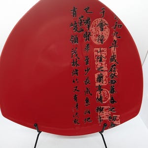 May include: A red ceramic plate with black calligraphy and a black metal stand. The calligraphy reads: "Some have mountains, some have forests, some have clear streams, and some have a collection of things."