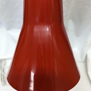 K&ouml;nnte beinhalten: Nahaufnahme eines roten, kegelf&ouml;rmigen Lampenschirms. Der Schirm hat eine gl&auml;nzende Oberfl&auml;che und eine glatte Oberfl&auml;che. Der Lampenschirm hat eine tiefe, satte rote Farbe.