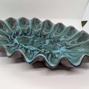 Può includere: Un grande piatto da portata ovale con un bordo ondulato. Il piatto è in ceramica e ha una glassa marmorea blu e verde.