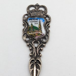 May include: A silver souvenir spoon with a shield displaying "WIEN STEPHANS-DOM" and a colourful image of St. Stephen's Cathedral. The spoon has an ornate handle and a crown-shaped top.