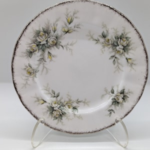 May include: A white porcelain plate with a silver rim and a floral design featuring white roses and green leaves.