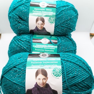 May include: Three skeins of teal blue yarn with silver glitter thread. The yarn label reads "Impeccable Glitter Paillettes Impeccables Purpurina Impecable" and includes a free pattern offer.
