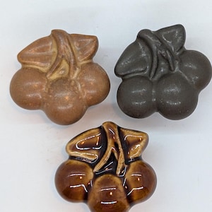 Peut inclure: Trois grappes de raisin en céramique dans différentes nuances de brun. Les raisins sont regroupés avec une feuille sur le dessus.