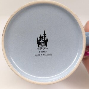 Op de afbeelding: Onderkant van een lichtblauwe keramische mok met een witte rand. De mok heeft een zwart silhouet van een kasteel met Mickey Mouse en de tekst "Walt Disney World", "&copy; Disney" en "MADE IN THAILAND".