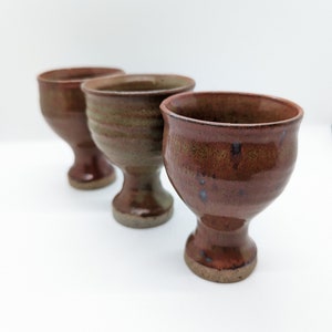 Könnte beinhalten: Drei Keramikbecher mit brauner und grüner Glasur. Die Becher haben einen breiten Boden und eine abgerundete Schalenform.