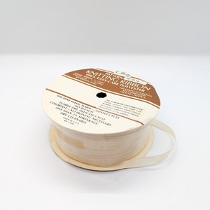 Könnte beinhalten: Eine Spule weißes Strickband aus 100 % pflegeleichtem Polyester. Das Etikett lautet "Muster # C0-0116 Strickband 100 % pflegeleichtes Polyester 100 Yards (91,4 Meter) Häkelnadel G empfohlen".