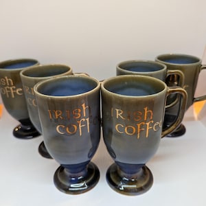 Puede incluir: Juego de seis tazas de café irlandés. Las tazas son de color verde oscuro con interior azul y base con pie. Las palabras "Irish Coffee" están impresas en dorado en la parte delantera de cada taza. Cada taza tiene un asa.