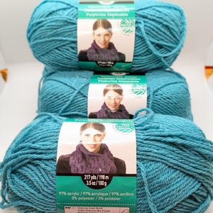 May include: Three skeins of teal blue yarn with silver glitter. The yarn label reads "Impeccable Glitter Purpurina Impecable" and lists the yarn content as 97% acrylic and 3% polyester. The label also states that the yarn is 217 yards and 3.5 ounces.