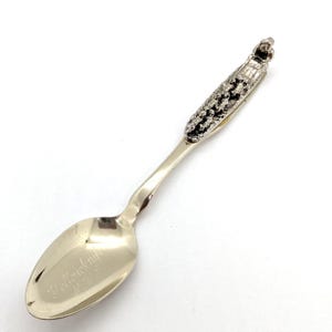 May include: A silver spoon with an ornate handle and the engraved text "Yellowknife N.W.T." on the bowl. The handle has a textured design and a small decorative element at the top, typical of souvenir spoons.
