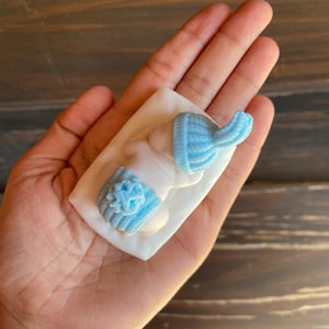 May include: Light blue baby hat and booties set. The miniature knit hat and booties are displayed on a white surface. The set is a soft, pastel blue color, perfect for a baby shower or newborn gift.