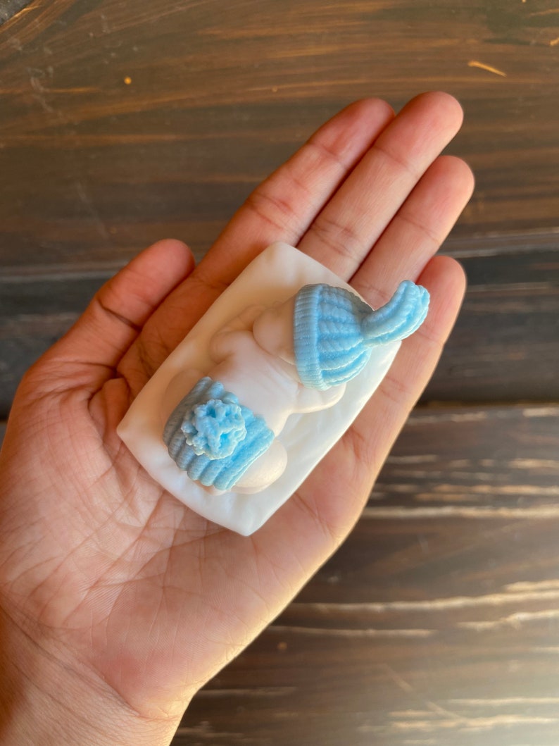 May include: Light blue baby hat and booties set. The miniature knit hat and booties are displayed on a white surface. The set is a soft, pastel blue color, perfect for a baby shower or newborn gift.