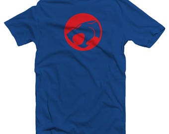 May include: Royal blue t-shirt featuring a red circle with a stylized cat head logo. The logo is centered on the chest of the shirt. The shirt has short sleeves and a crew neck.