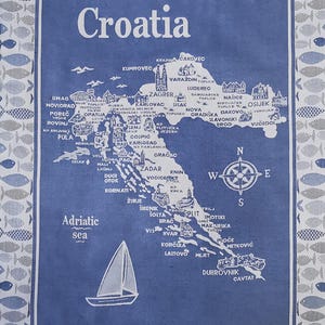 May include: Blue and white decorative towel featuring a map of Croatia with city names and a sailboat illustration. The word "Croatia" is at the top, and the Adriatic Sea is labeled. The border has a pattern of fish.