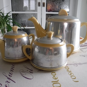 May include: A vintage silver tea set with yellow accents. The set includes a teapot, sugar bowl, and creamer.